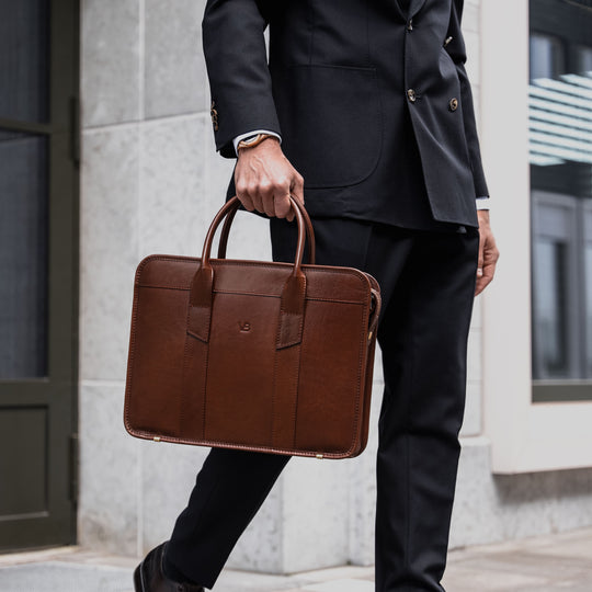 An exquisite, slim, brown Von Baer full-grain leather laptop briefcase held by a man in a suit