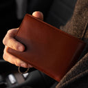 Von Baer Harrington large full-grain leather passport wallet in brown held in hand inside a car, travel wallet for passport and cards.