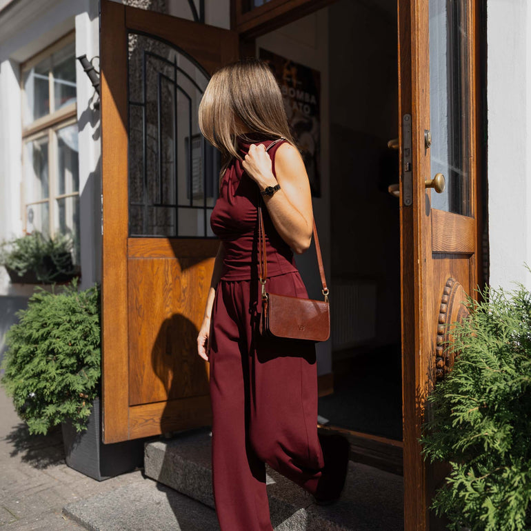 Brown Von Baer Isabella leather women's handbag, with a woman going out from a cafe with wooden doors