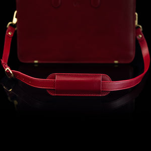 A red Von Baer leather shoulder bag strap is shown on a leather bag.