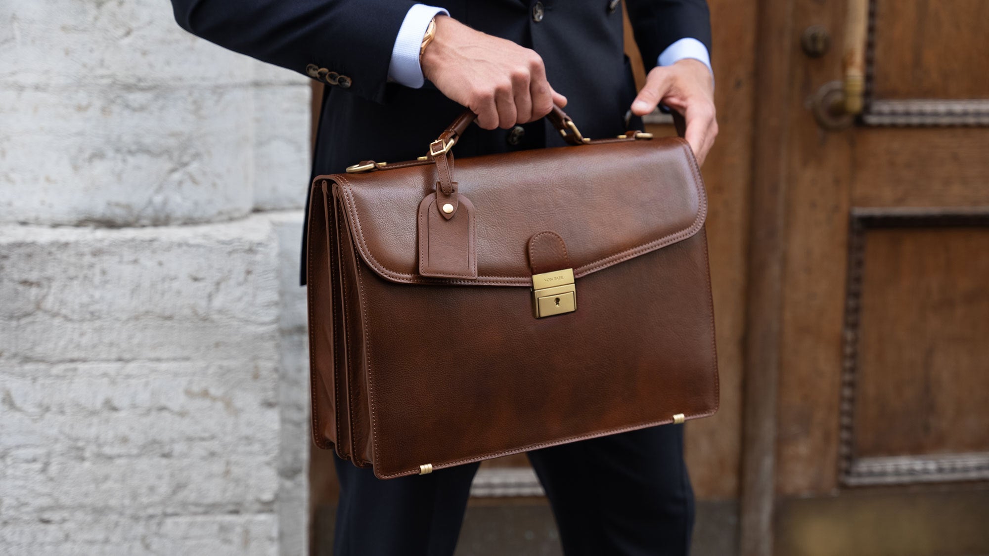 A large, brown Von Baer No.1 luxury high-quality men's leather briefcase for work and documents, held by a man in a suit