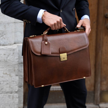 A large, brown Von Baer No.1 full-grain leather briefcase for work and documents with a luggage tag, held by a man in a suit