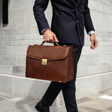 A large, brown Von Baer No.1 luxury men's leather briefcase for work and documents, held by a man in a suit