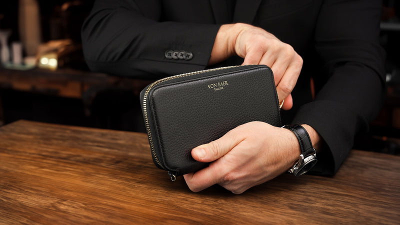 Von Baer origin luxury RFID men’s leather wallet in black held by a male model in a café shop, premium wallet for professionals.