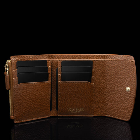 Von Baer Reverie compact cognac pebbled leather wallet for women, open to showcase card slots, interior pockets, and gold-tone snap closure against a reflective black background
