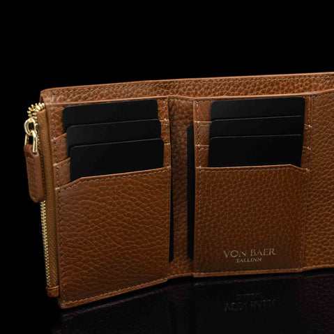 Von Baer Reverie luxury small cognac pebbled leather wallet for women, open to showcase eight card slots, black cards, a gold-tone zipper pull, and the debossed brand logo on the interior against a black background