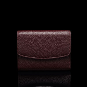 Von Baer Reverie compact burgundy pebbled leather wallet for women with a fold-over flap, shown centered in a front view against a solid black background with a subtle reflection.