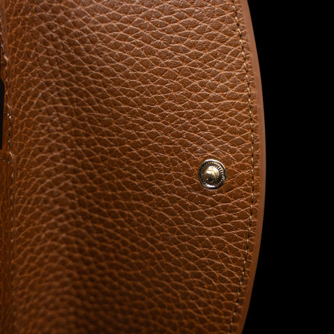 Von Baer Reverie small cognac pebbled leather wallet for women, shown in close-up highlighting the round metallic snap-button closure against a black background