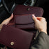 Von Baer Reverie burgundy pebbled compact leather women's wallet and Isabella small leather crossbody bag, shown in close-up inside a car, highlighting the open wallet's interior, snap-button closure, and small zippered pocket