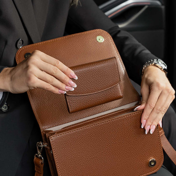 Von Baer Reverie women's full-grain compact leather wallet and Isabella Grande large cognac leather crossbody bag, shown open in a close-up to highlight the pebbled leather texture and spacious interior compartments, held by a woman wearing a black blazer