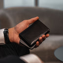 Von Baer Tallinn Grant leather card case in black held by a male model in a luxury hotel
