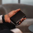 Von Baer Tallinn Grant leather card case in black held by a male model in a luxury hotel