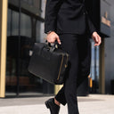 Person in a black suit holding a black briefcase outside a building.