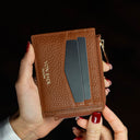 Brown leather card holder wallet with card slots held by a hand against a black background